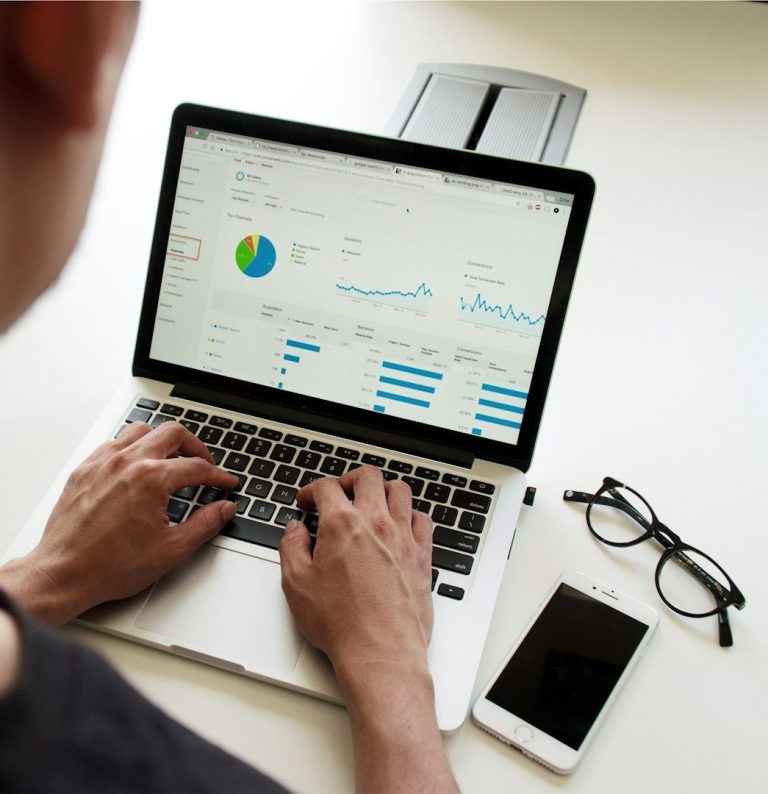 Person nutzt Laptop zur Analyse von Daten, daneben ein Smartphone und Brille.
